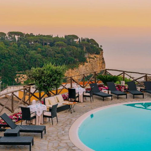 Terrasse panoramique avec piscine et chaises longues face aux falaises de Scala.
