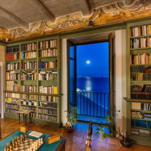 Bibliothèque historique du Palazzo Suriano avec vue sur la mer éclairée par la lune.