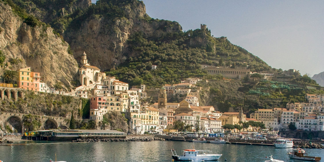 Vue panoramique depuis la mer sur le port d'Amalfi, ses bateaux amarrés et ses maisons accrochées aux falaises.