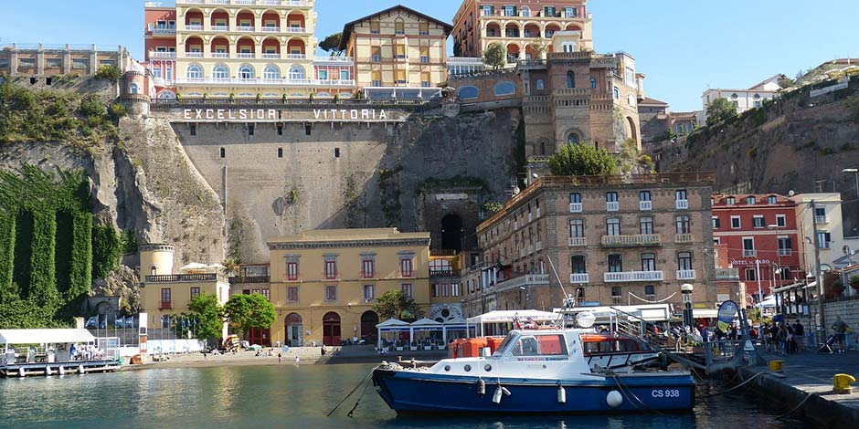 Port de Sorrente avec bateaux, hôtels sur la falaise et accès vers le centre-ville.