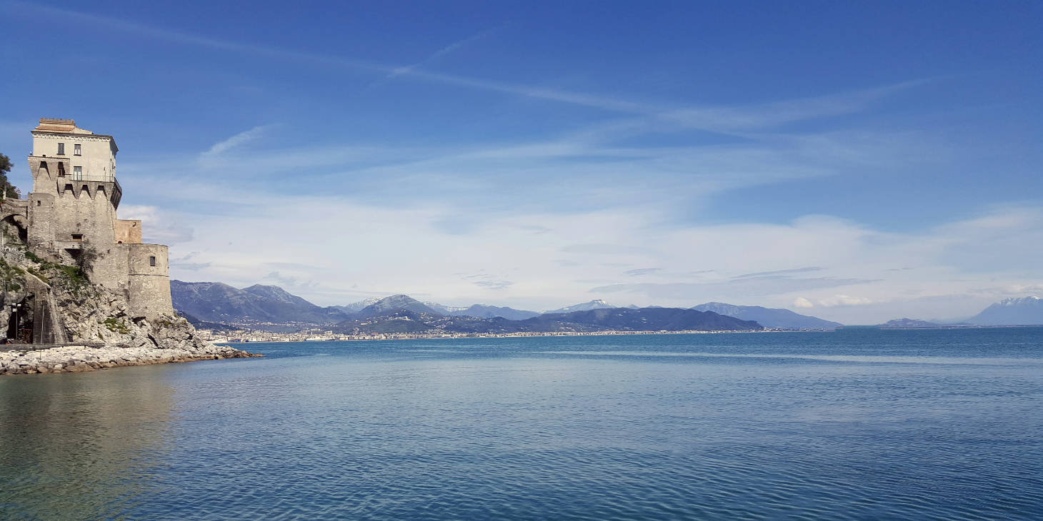La tour de guet de Cetara surplombant l'eau turquoise avec les côtes montagneuses au loin.