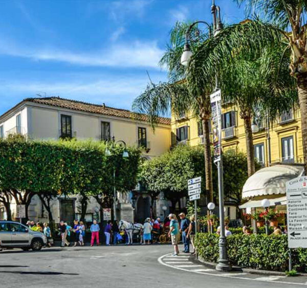 Piazza Tasso à Sorrente avec cafés, palmiers, passants et bâtiments colorés.