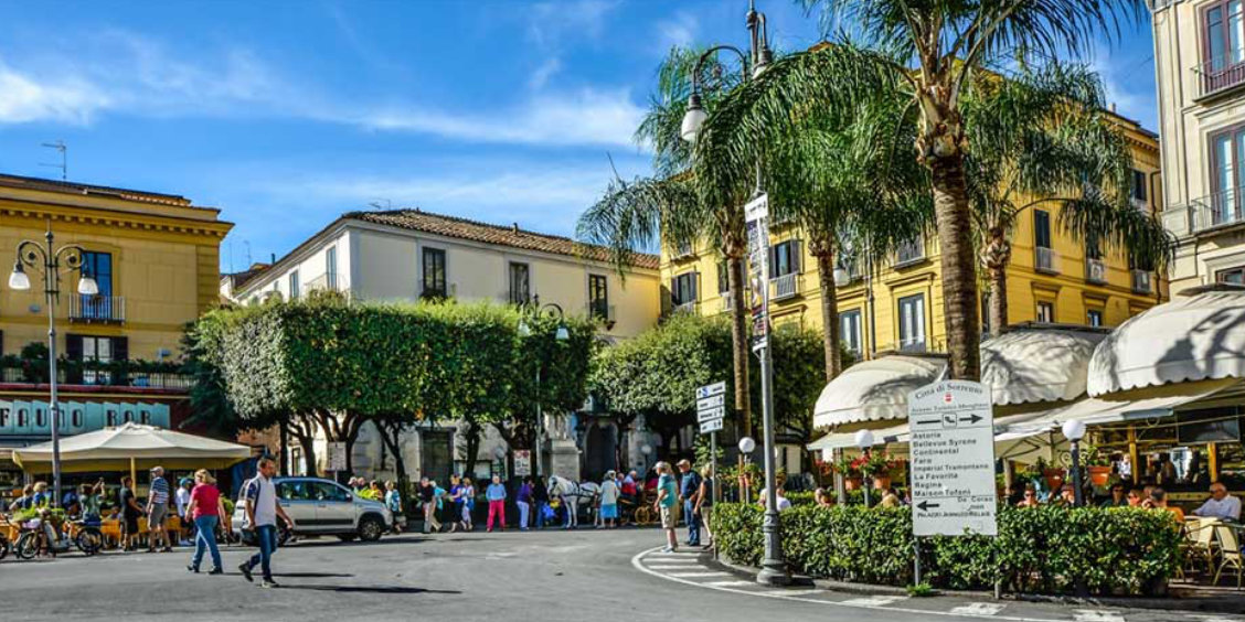 Piazza Tasso à Sorrente avec cafés, palmiers, passants et bâtiments colorés.