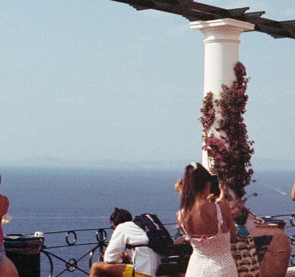Terrasse panoramique à Capri avec des colonnes blanches ornées de bougainvilliers et des visiteurs admirant la vue sur la mer Méditerranée.