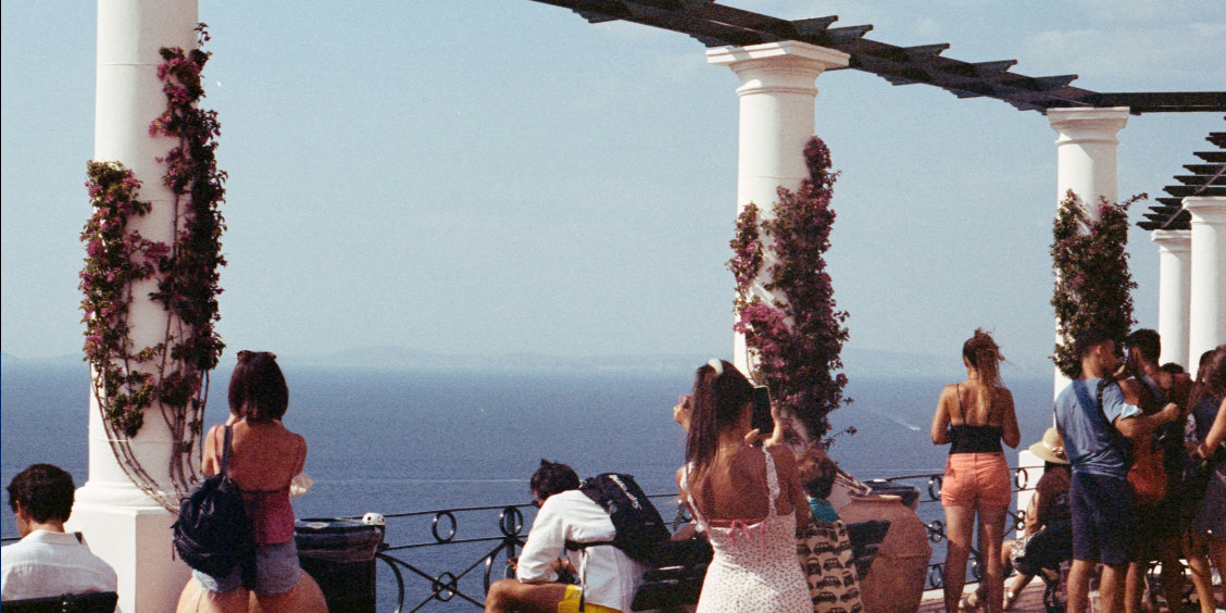 Terrasse panoramique à Capri avec des colonnes blanches ornées de bougainvilliers et des visiteurs admirant la vue sur la mer Méditerranée.