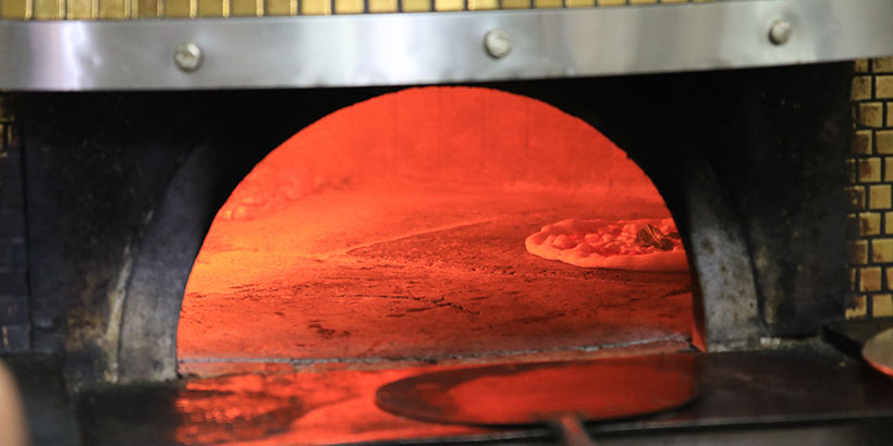 Pizza napolitaine en train de cuire dans un four à bois traditionnel avec des flammes vives en arrière-plan.
