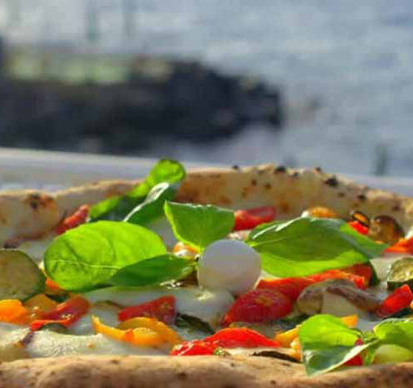 Pizza napolitaine à Sorrente avec légumes colorés, basilic et vue sur la mer.