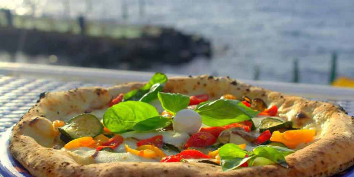 Pizza napolitaine à Sorrente avec légumes colorés, basilic et vue sur la mer.