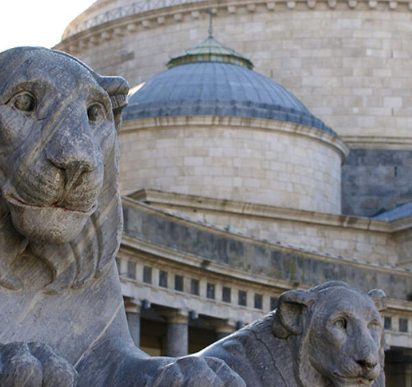 Statues de lions sur la place du Plébiscite avec la basilique en arrière-plan à Naples.