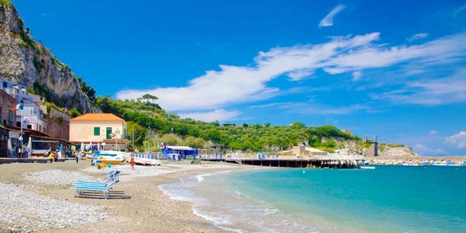 Plage de Baia di Puolo près de Sorrente avec sable, mer turquoise et petit port.