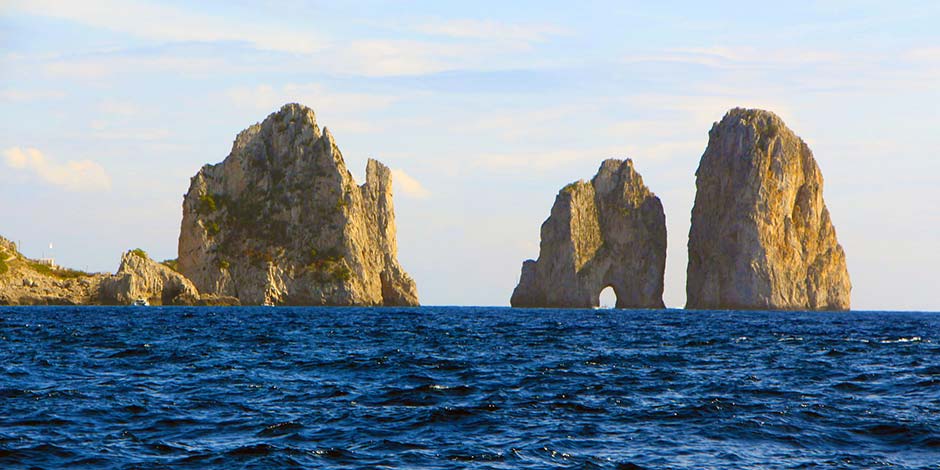 Les trois célèbres rochers Faraglioni de Capri émergeant d'une mer bleue profonde sous un ciel clair.