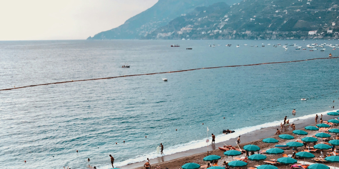 Longue plage de sable fin à Maiori avec de nombreux parasols turquoises.