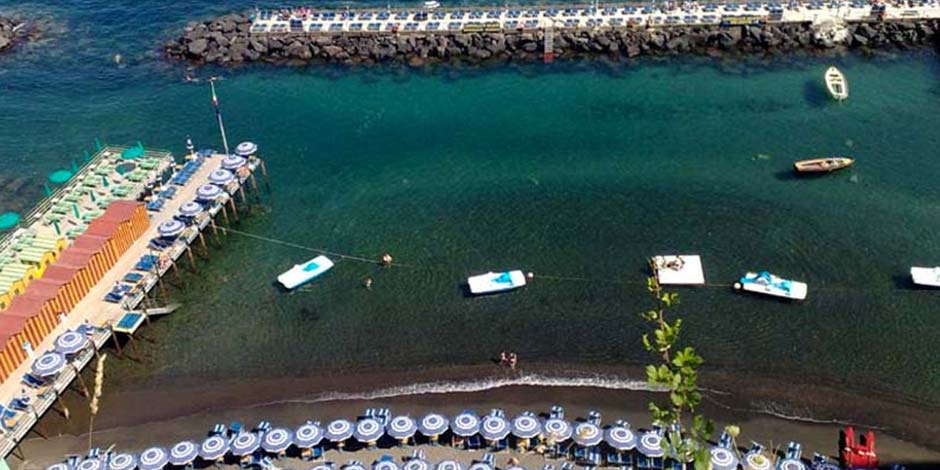 Plage de Marina Piccola à Sorrente avec parasols, pontons et bateaux sur l’eau claire.