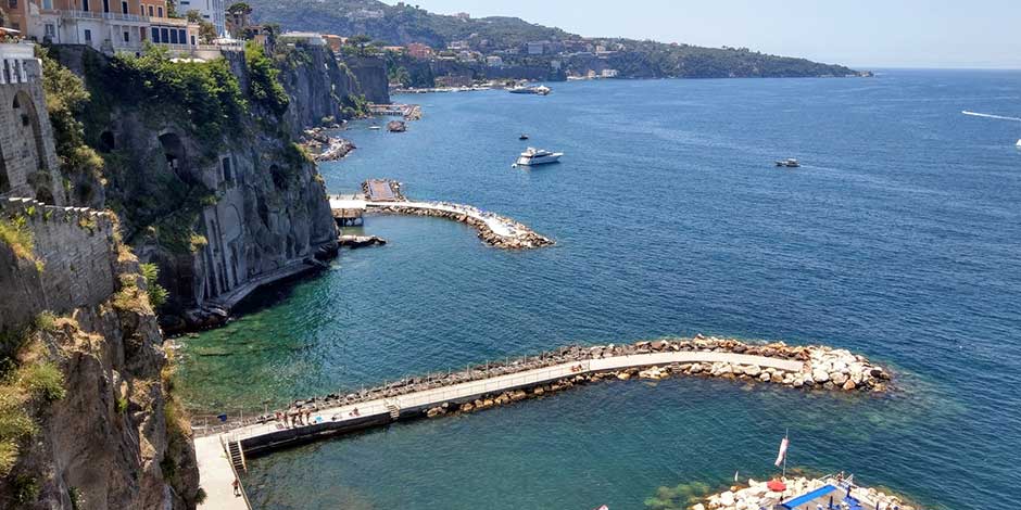 Plage de Marinella à Sant’Agnello avec pontons, falaises et mer bleue près de Sorrente.
