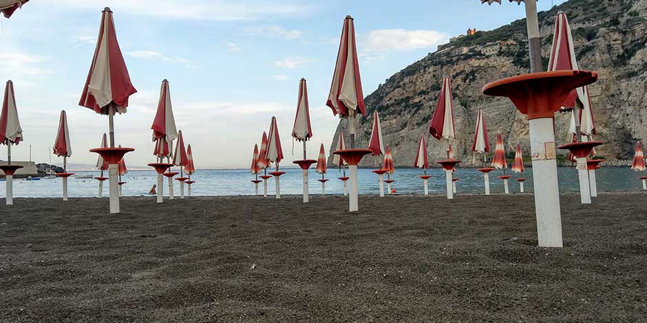 Plage de Meta près de Sorrente avec parasols rouges, sable sombre et falaises en arrière-plan.