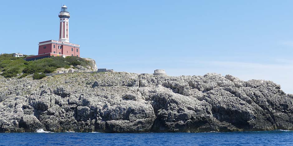 Phare rouge de Punta Carena à Capri sur sa falaise rocheuse bordant la mer bleue.