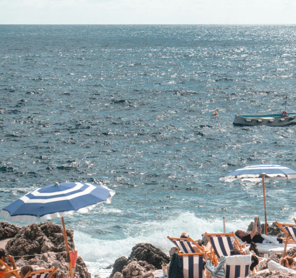 Chaises longues et parasols à rayures bleues et blanches sur une plage rocheuse à Capri avec la mer en arrière-plan.
