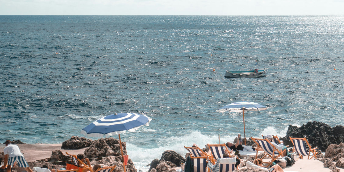 Chaises longues et parasols à rayures bleues et blanches sur une plage rocheuse à Capri avec la mer en arrière-plan.