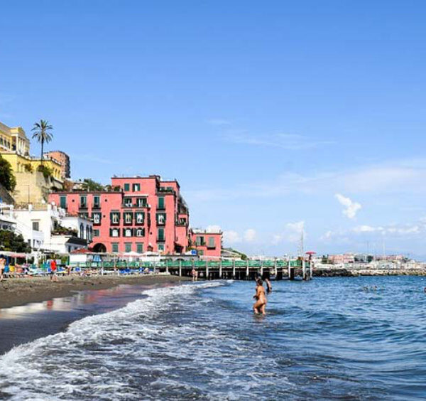 Plage de Naples avec maisons colorées, mer calme et vue sur le Vésuve le long du littoral.