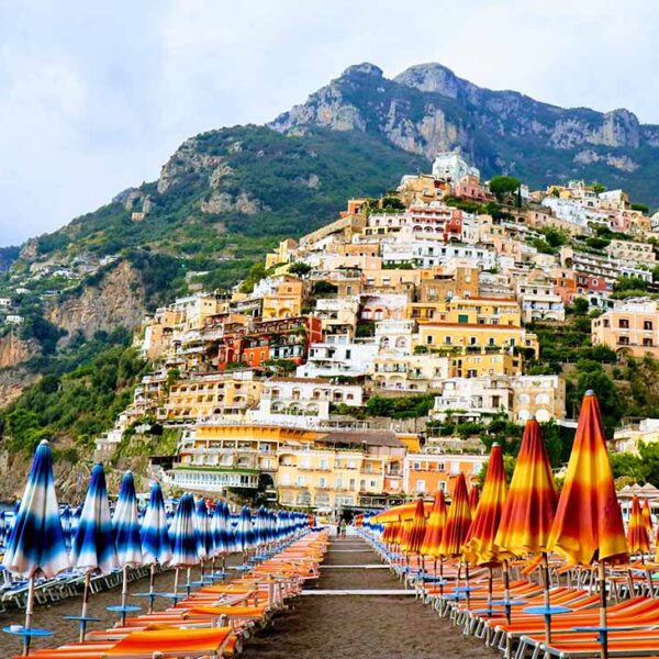 Plage de Positano avec rangées de parasols colorés et maisons accrochées à la montagne.