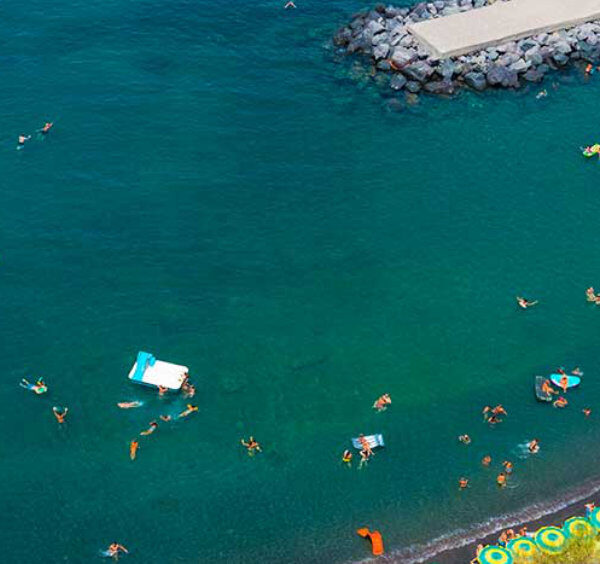Plage de Sorrente vue d’en haut avec baigneurs, matelas flottants et eau turquoise.