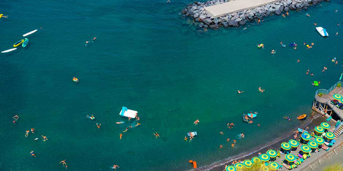 Plage de Sorrente vue d’en haut avec baigneurs, matelas flottants et eau turquoise.