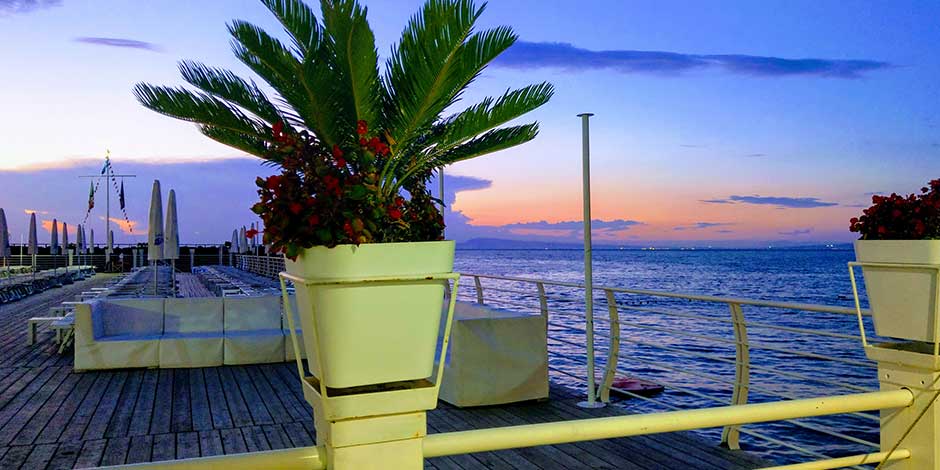 Plage de Piano di Sorrento au coucher du soleil avec terrasse, palmiers et vue sur la mer.