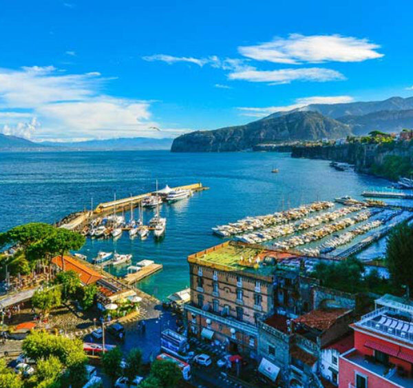 Port de Sorrente avec bateaux, falaises et vue sur le Vésuve dans le golfe de Naples.