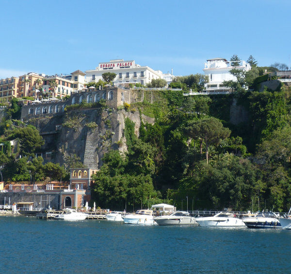 Port de Sorrente avec bateaux amarrés, falaises verdoyantes et hôtels panoramiques.