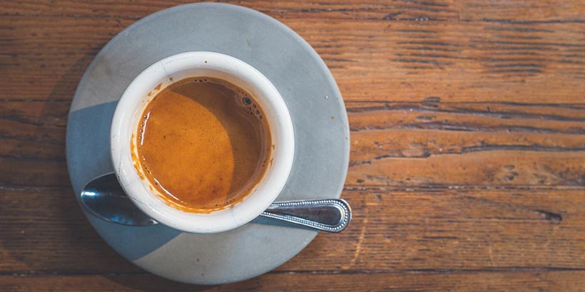 Vue de dessus d'une tasse d'expresso avec une mousse onctueuse, posée sur une soucoupe avec une petite cuillère sur une table en bois rustique.