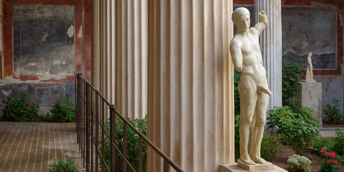 Statue de Priape adossée à une colonne cannelée dans une cour antique de Pompéi.