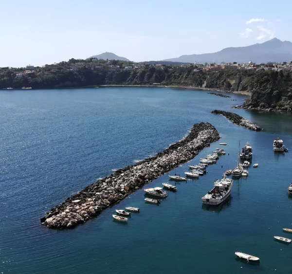 Vue aérienne du port de Corricella sur l'île de Procida avec ses bateaux et les falaises verdoyantes en arrière-plan.