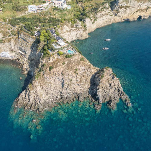 Vue aérienne spectaculaire de l'hôtel Punta Chiarito Resort perché sur une falaise surplombant des eaux cristallines.