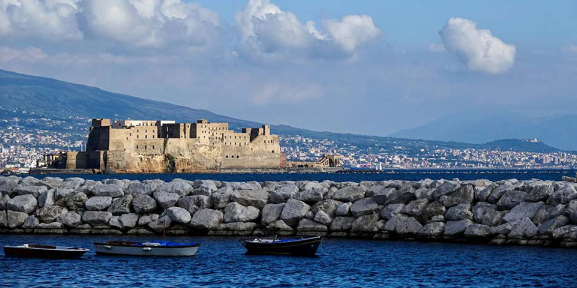 Le Castel dell'Ovo dominant le front de mer de Naples avec des barques au premier plan.
