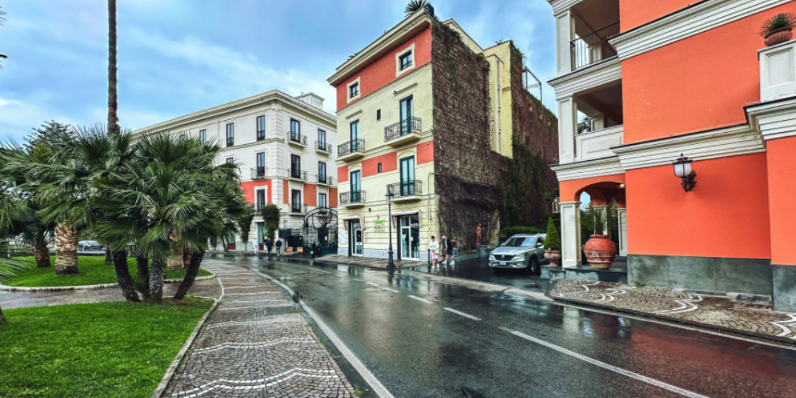 Rue de Sorrente sous la pluie avec façades colorées, palmiers et chaussée mouillée.
