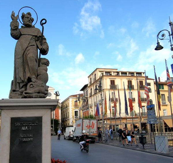 Statue de Sant’Antonino à Sorrente avec rue animée, passants et bâtiments du centre.