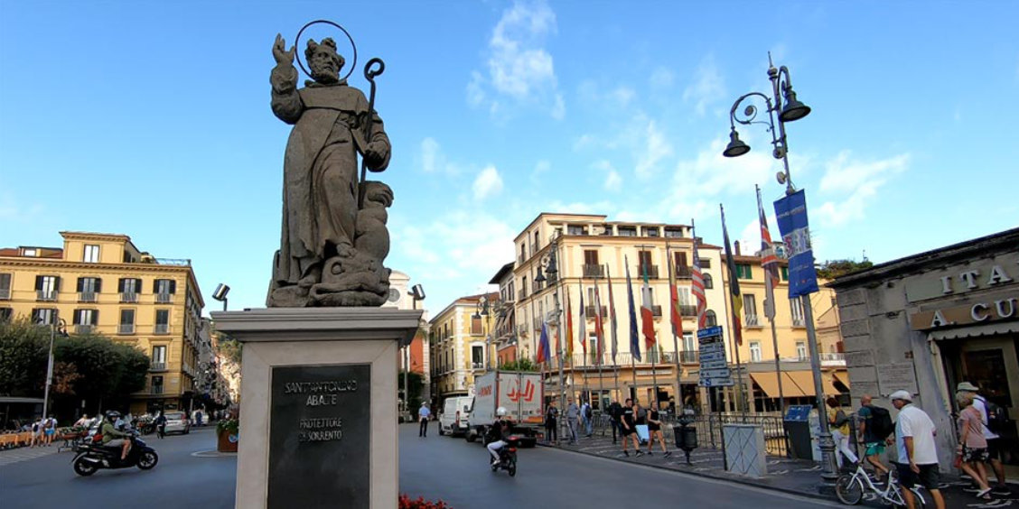 Statue de Sant’Antonino à Sorrente avec rue animée, passants et bâtiments du centre.