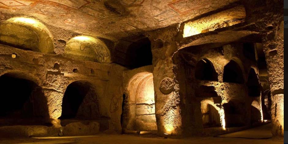 Chambres funéraires des catacombes de San Gennaro à Naples, avec niches creusées dans la roche et fresques anciennes éclairées.