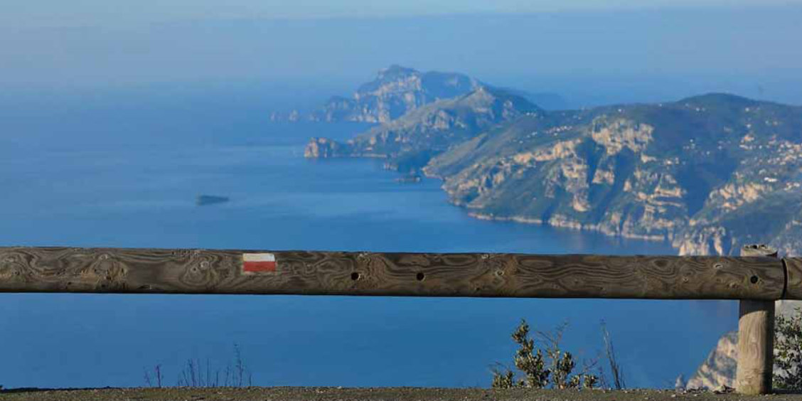Vue panoramique de randonnée près de Sorrente avec mer bleue, falaises et côte au loin.