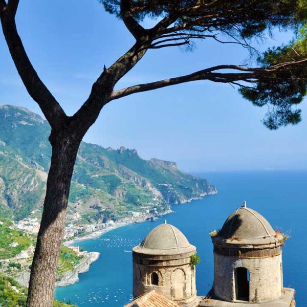 Vue panoramique sur la mer Méditerranée et la Côte Amalfitaine depuis les jardins de Ravello, avec un pin parasol et les dômes de la Villa Rufolo.