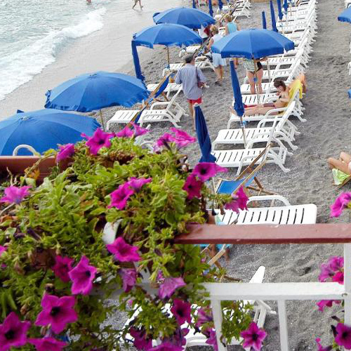Plage privée avec parasols bleus et transats vue depuis une terrasse fleurie à Maiori.