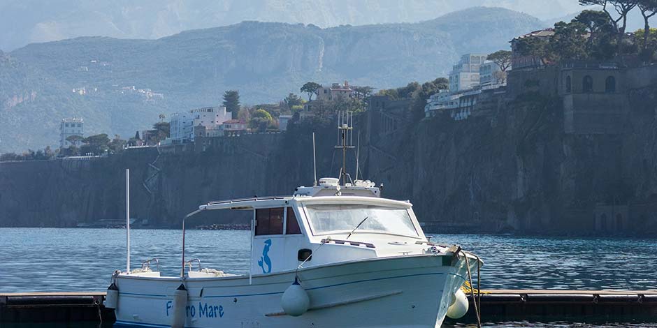 Bateau amarré au port de Sorrente avec les falaises de la côte en arrière-plan.