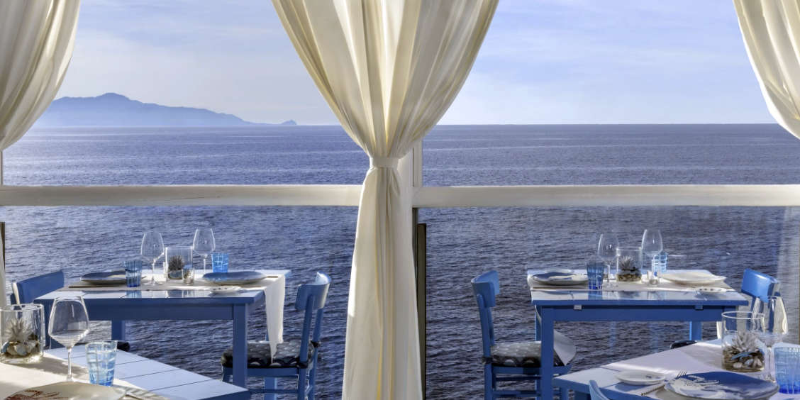 Vue sur la mer Méditerranée depuis la terrasse face à l'eau del restaurant de prestige Il Riccio à Anacapri, con des tables dressées pour un dîner d'exception.