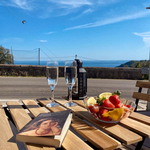 Table en bois avec verres de vin pétillant, fruits et livre face à la mer.