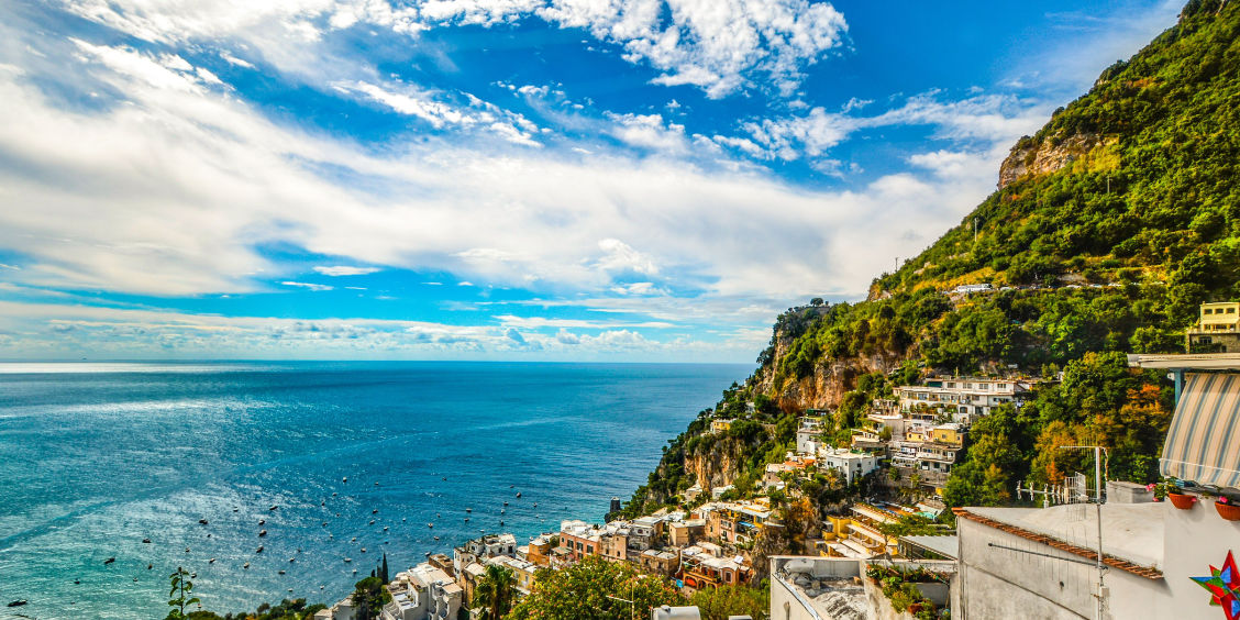 anorama sur la côte de Positano avec bateaux en mer sous un ciel ensoleillé.