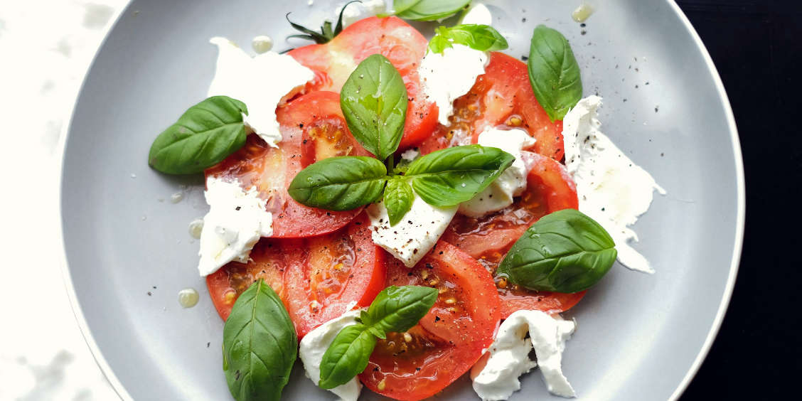 Salade Caprese traditionnelle avec tranches de tomates mûres, mozzarella fraîche et feuilles de basilic sur une assiette grise.