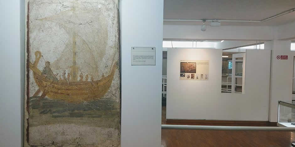 Fresque murale antique représentant un bateau à voile dans une salle d'exposition du musée.