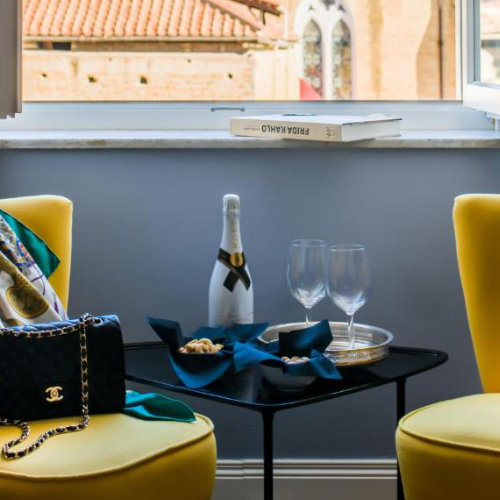 Coin détente élégant avec deux fauteuils jaunes, une bouteille de champagne sur une petite table noire et un livre sur Frida Kahlo posé sur le rebord de la fenêtre.
