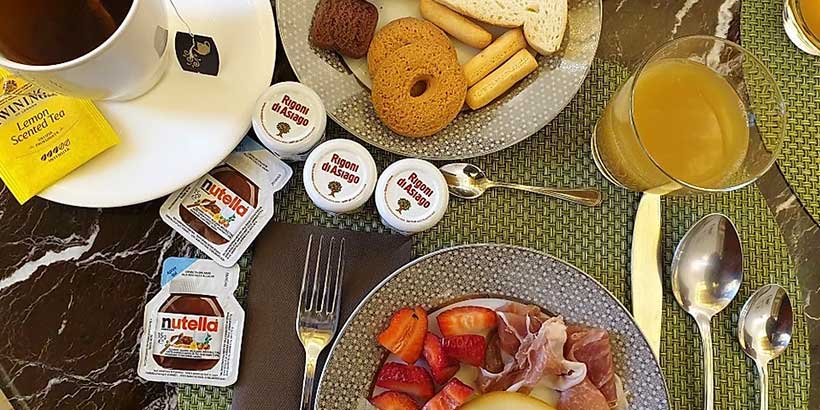 Petit-déjeuner à Naples avec thé, jus d’orange, viennoiseries, fruits et confitures, servi dans un hôtel.