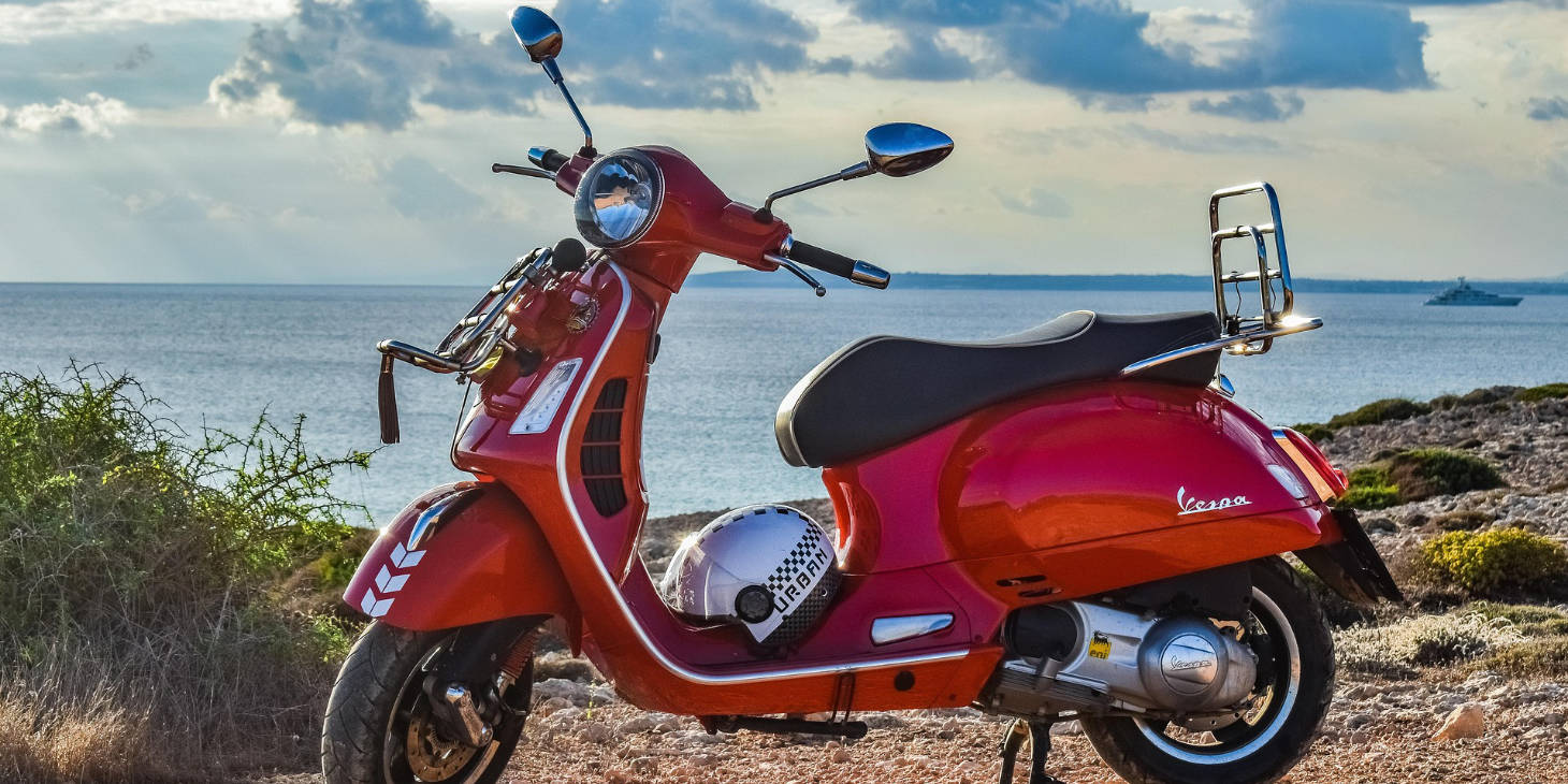 Vespa rouge garée sur la côte d'Ischia face à la mer.